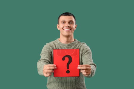 Photo for Young man holding paper with question mark on green background - Royalty Free Image