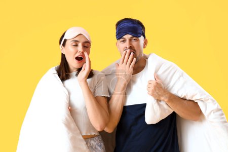 Photo for Sleepy young couple with masks and blanket on yellow background - Royalty Free Image