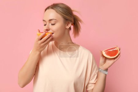 Photo for Young woman eating grapefruit on pink background - Royalty Free Image