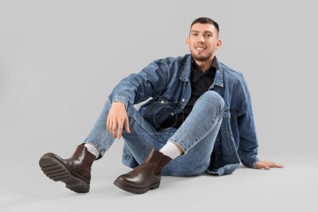 Photo for Stylish young man in denim clothes sitting on light background - Royalty Free Image