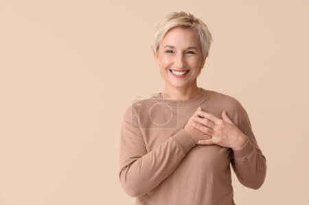 Foto de Mujer madura sonriente revisando su pecho sobre fondo beige. Concepto de concienciación - Imagen libre de derechos