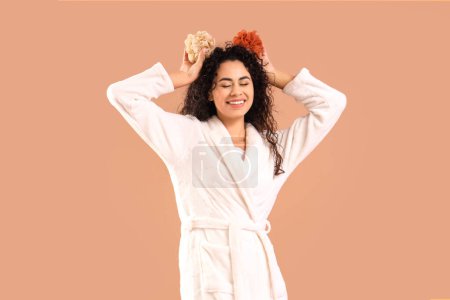 Photo for Young African-American woman in bathrobe with loofahs on brown background - Royalty Free Image