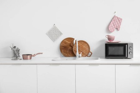 Foto de Interior de la cocina luminosa con horno microondas, lavabo y utensilios en mostradores blancos - Imagen libre de derechos