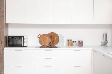 Foto de Interior de la cocina luminosa con horno microondas, cocina eléctrica y utensilios en mostradores blancos - Imagen libre de derechos