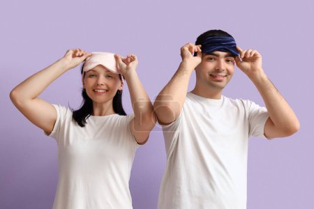 Téléchargez les photos : Jeune couple avec des masques de couchage sur fond lilas - en image libre de droit