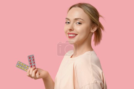 Photo for Young woman with blisters of vitamin A pills on pink background - Royalty Free Image