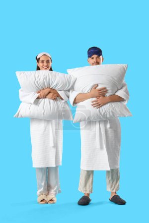 Téléchargez les photos : Jeune couple avec des oreillers doux sur fond bleu - en image libre de droit