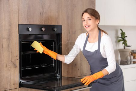 Photo for Female janitor cleaning electric oven with sponge in kitchen - Royalty Free Image