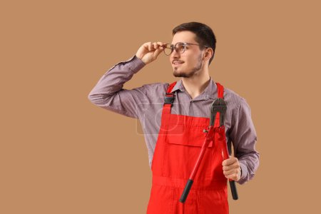 Photo for Young male worker in eyeglasses with bolt cutter on beige background - Royalty Free Image