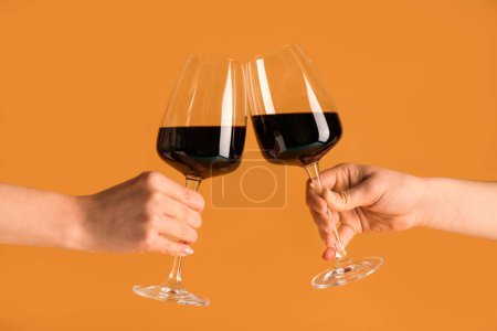 Téléchargez les photos : Mains féminines avec verres de vin rouge sur fond orange - en image libre de droit
