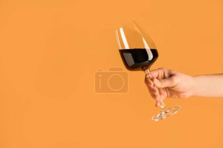 Téléchargez les photos : Main féminine avec verre de vin rouge sur fond orange - en image libre de droit