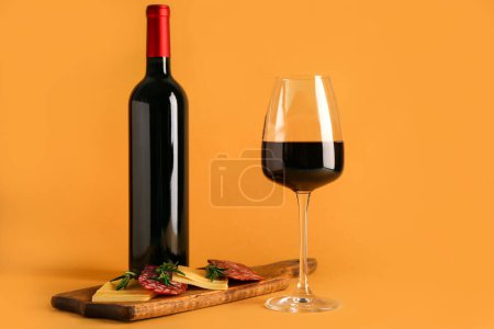 Téléchargez les photos : Bouteille et verre de vin rouge avec collations sur fond orange - en image libre de droit
