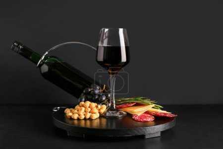 Téléchargez les photos : Bouteille et verre de vin rouge avec collations sur fond noir - en image libre de droit
