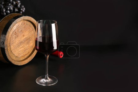 Téléchargez les photos : Verre de vin rouge avec tonneau et raisins sur fond noir - en image libre de droit