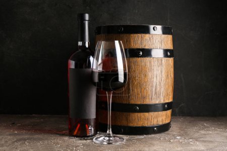 Téléchargez les photos : Bouteille et verre de vin rouge avec tonneau sur table grise sur fond grunge noir - en image libre de droit