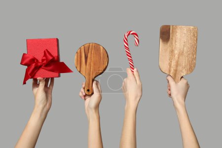 Foto de Manos femeninas con tablas de cortar de madera, regalo de Navidad y bastón de caramelo sobre fondo gris - Imagen libre de derechos