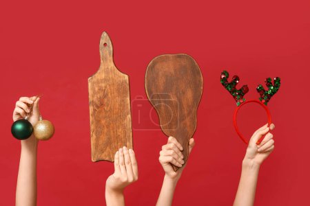 Foto de Manos femeninas con tablas de cortar de madera, bolas de Navidad y diadema de reno sobre fondo rojo - Imagen libre de derechos