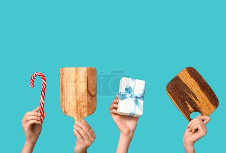 Foto de Manos femeninas con tablas de cortar de madera, regalo de Navidad y bastón de caramelo sobre fondo azul - Imagen libre de derechos