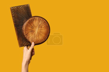 Foto de Mano femenina con tablas de cortar de madera sobre fondo amarillo - Imagen libre de derechos