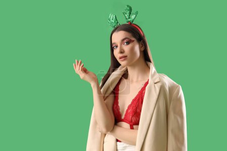 Beautiful young woman in Christmas deer horns on green background