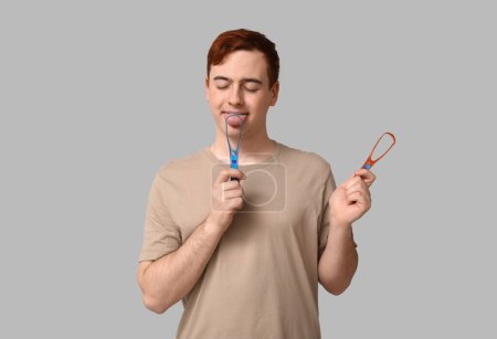 Téléchargez les photos : Jeune homme avec grattoirs de langue sur fond gris - en image libre de droit