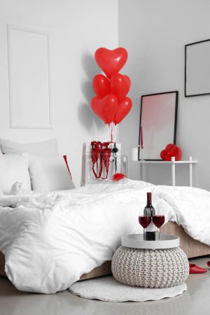 Foto de Interior de dormitorio luminoso con copas de vino, globos en forma de corazón y lencería roja en bolsa de compras. Celebración de San Valentín - Imagen libre de derechos
