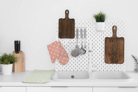Téléchargez les photos : Comptoirs de cuisine blancs avec planches à découper, pegboard, évier et ustensiles - en image libre de droit