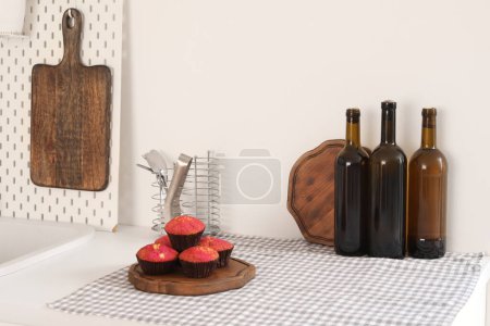 Téléchargez les photos : Planche à découper avec muffins et bouteilles de vin sur comptoir de cuisine blanc - en image libre de droit