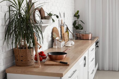 Foto de Mostrador de madera con tablas de cortar, planta de interior, maniquí y sartén en la cocina moderna - Imagen libre de derechos