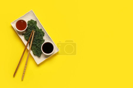 Foto de Placa con algas sanas, salsas y palillos sobre fondo amarillo - Imagen libre de derechos