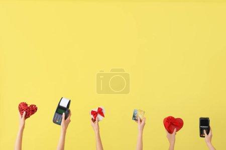 Women with gifts, payment terminals and credit cards on yellow background. Valentine's Day celebration