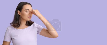 Young woman touching her nose on lilac background with space for text