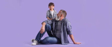 Foto de Cute little boy with grandfather on purple background - Imagen libre de derechos