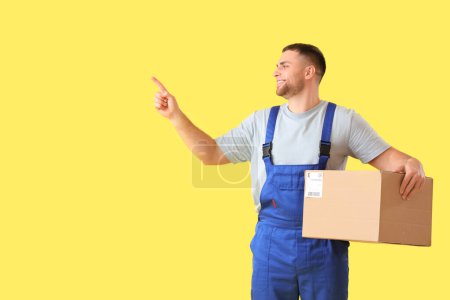 Photo for Male courier with parcel pointing at something on yellow background - Royalty Free Image