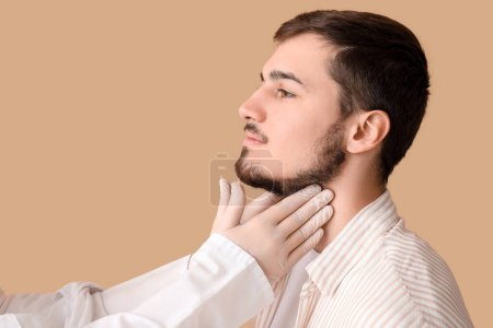 Photo for Endocrinologist examining thyroid gland of young man on beige background - Royalty Free Image
