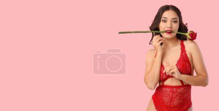 Pretty young woman in sexy lingerie holding beautiful rose in mouth on pink background with space for text