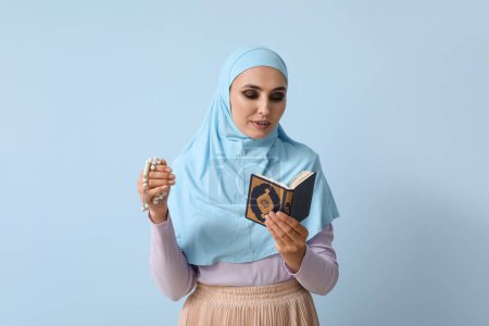 Téléchargez les photos : Young Muslim woman with Koran and prayer beads on blue background. Islamic New Year celebration - en image libre de droit