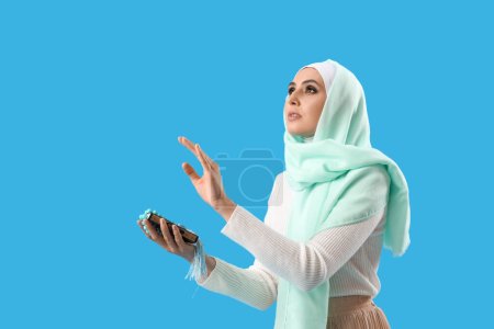 Téléchargez les photos : Young Muslim woman with Koran and prayer beads on blue background. Islamic New Year celebration - en image libre de droit