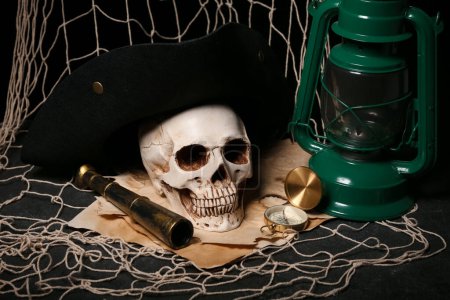 Téléchargez les photos : Crâne humain avec verre espion, lampe à huile, chapeau pirate et filet sur fond noir - en image libre de droit
