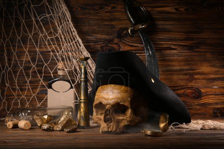 Téléchargez les photos : Crâne humain avec chapeau pirate, pépites d'or, bouteille de rhum et équipement de voyage sur fond de bois brun - en image libre de droit