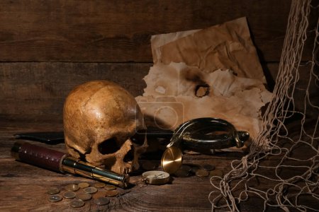 Téléchargez les photos : Crâne humain avec verre espion, épée, boussole et pièces sur fond brun en bois - en image libre de droit