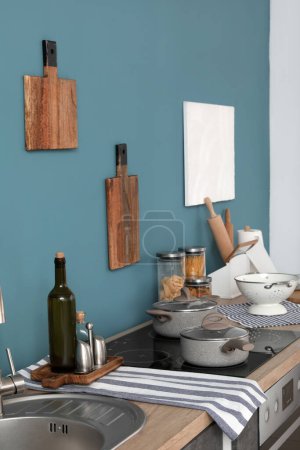 Foto de Electric stove with cooking pots and cutting boards hanging on blue wall in modern kitchen - Imagen libre de derechos