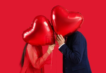 Téléchargez les photos : Couple with heart-shaped air balloons for Valentine's day on red background - en image libre de droit