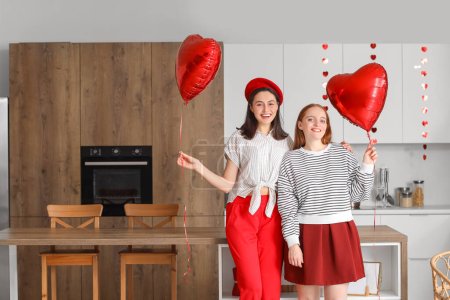 Foto de Young lesbian couple with heart-shaped balloons in kitchen on Valentine's Day - Imagen libre de derechos