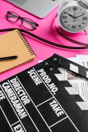 Photo for Notebook with movie clapper, film reel and alarm clock on pink background - Royalty Free Image