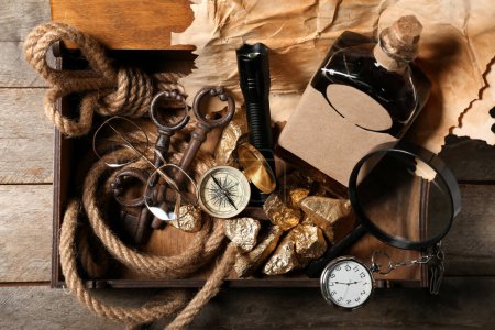 Téléchargez les photos : Boîte avec équipement de voyage, pépites d'or et bouteille de rhum sur fond de bois brun - en image libre de droit