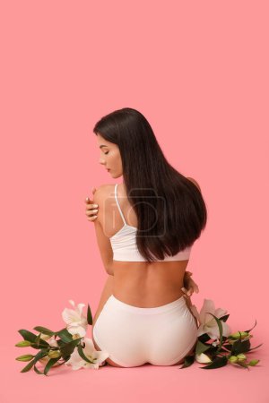Beautiful young woman with white lily flowers sitting on pink background