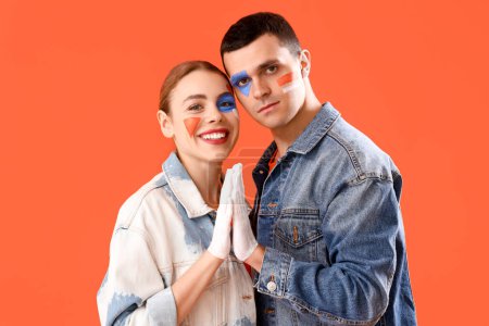 Téléchargez les photos : Jeune couple avec des visages peints tenant la main sur fond orange - en image libre de droit