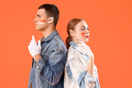 Téléchargez les photos : Jeune couple avec des visages peints sur fond orange - en image libre de droit