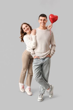 Feliz pareja joven con globo aerostático en forma de corazón sobre fondo rosa. Celebración de San Valentín